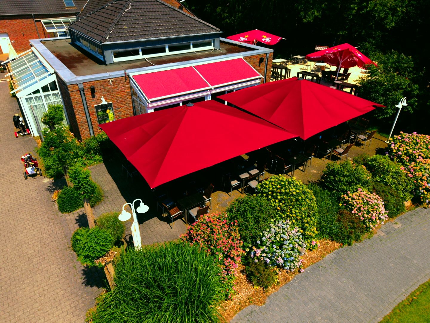 Luftaufnahme der Terrasse des Treff.clubhaus2 mit roten Sonnenschirmen am Golfclub Niep