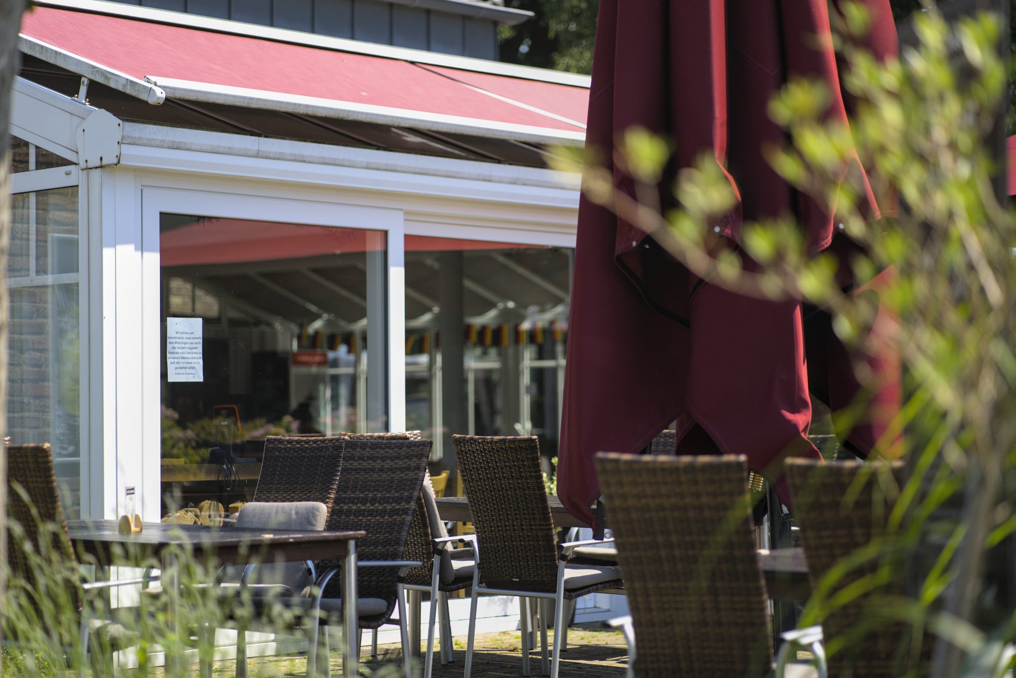 Die sonnige Terrasse des Treff.clubhaus2 am Golfclub Niep mit roten Sonnenschirmen